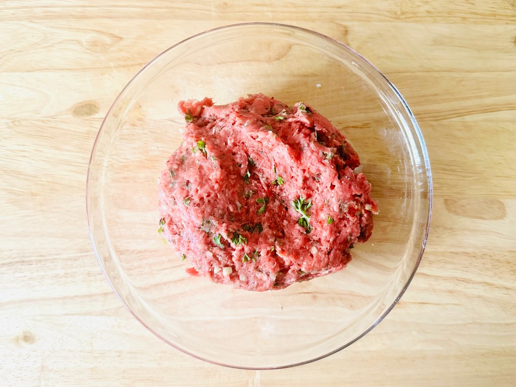 Bowl full of ground beef, garlic, parsley, and seasonings mixed together