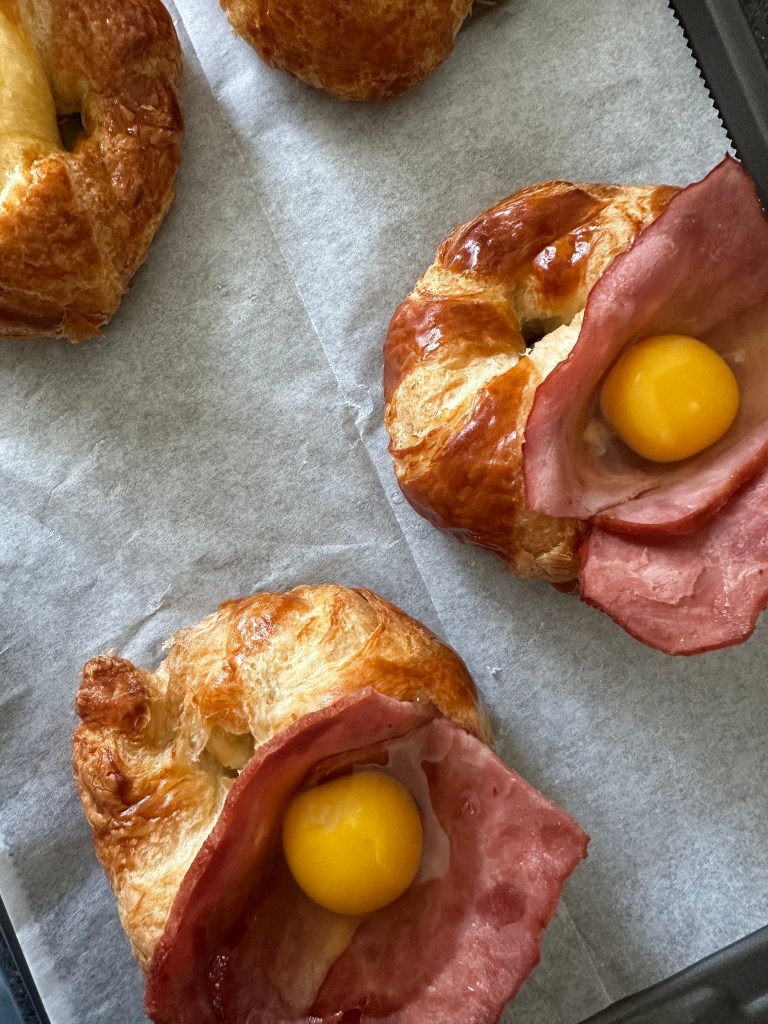 Croissants on a parchment paper-lined baking sheet, topped with slices of turkey bacon and eggs