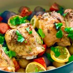 A pan with baked lemon chicken thighs and potatoes with lemon slices