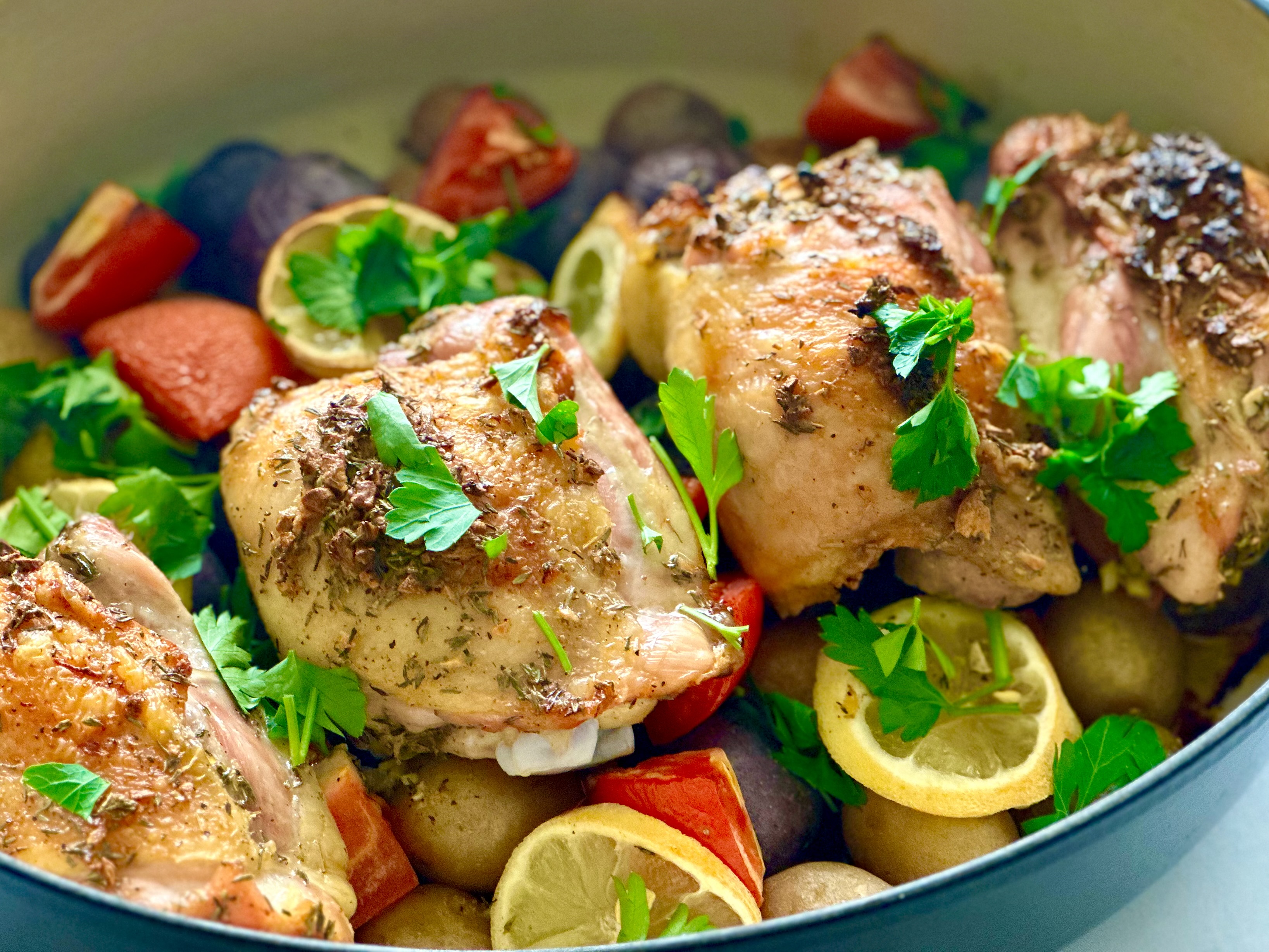 A pan with baked lemon chicken thighs and potatoes with lemon slices