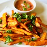 A plate of homemade sweet potato fries garnished with parsley and served with a side of dipping sauce