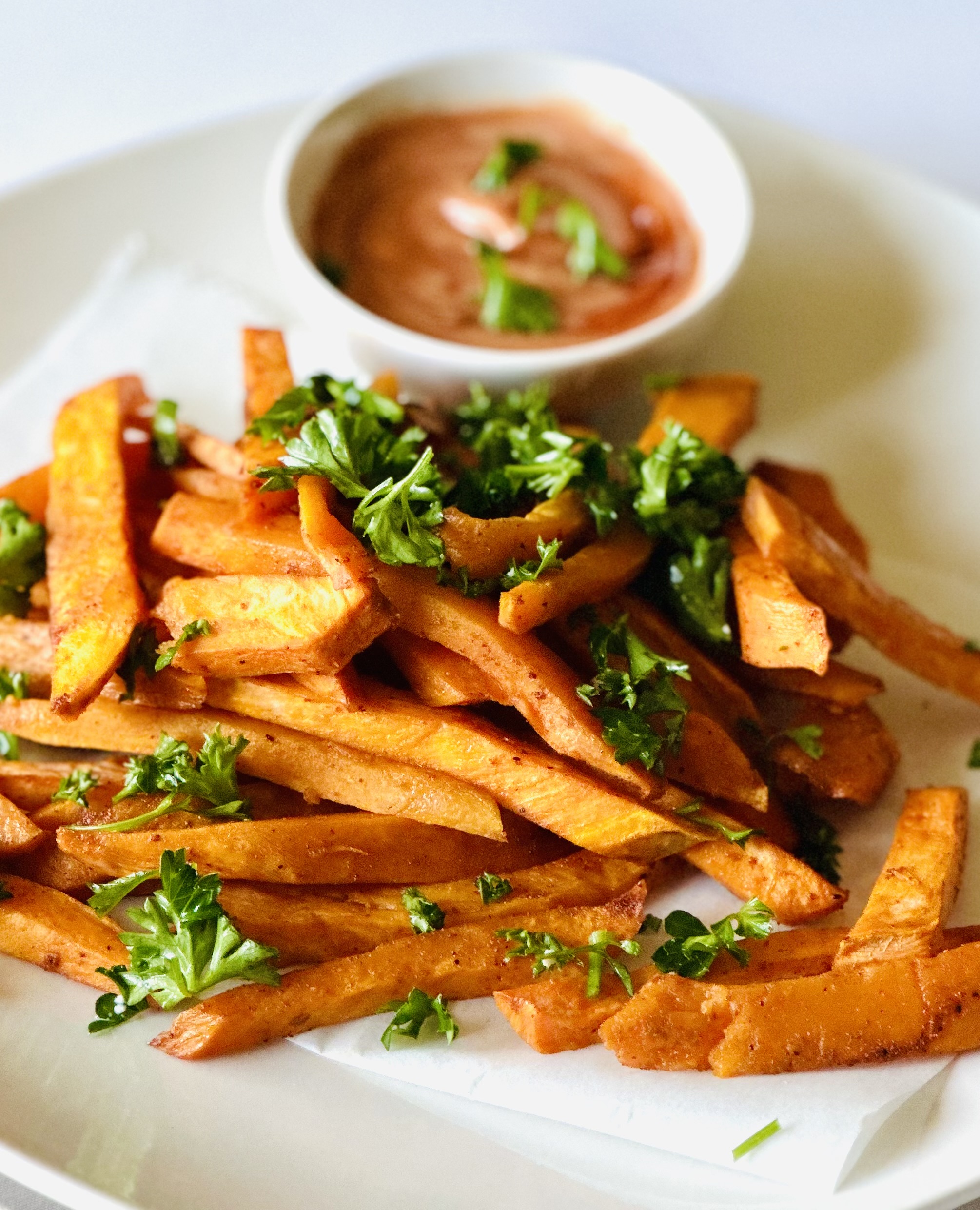 A plate of homemade sweet potato fries garnished with parsley and served with a side of dipping sauce