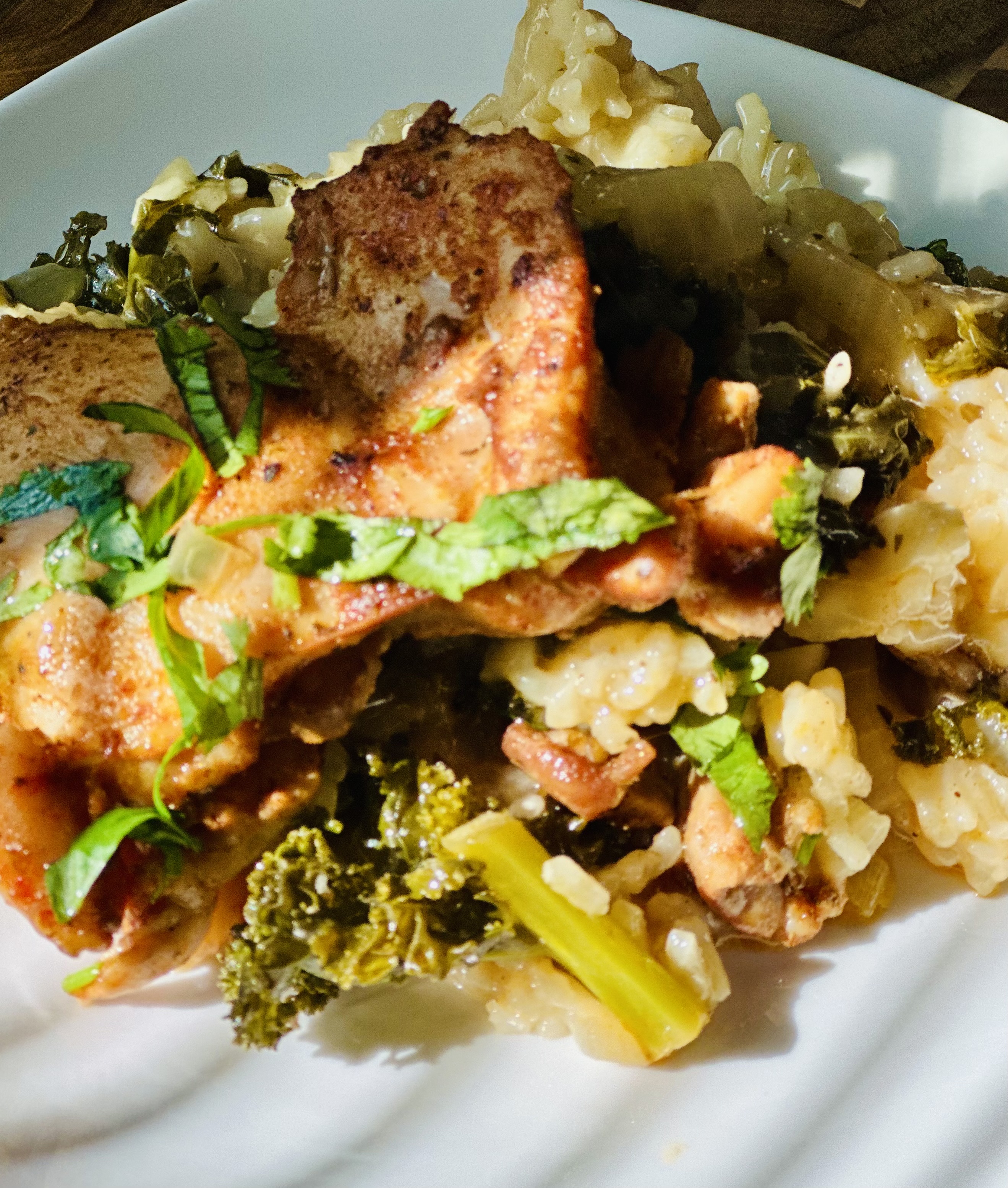 Shot of a plate with a base of rice, kale, and vegetables and baked chicken thighs sitting on top