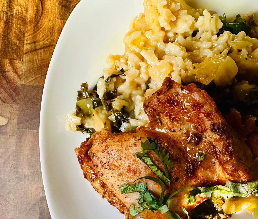 Shot of a plate with a base of rice, kale, and vegetables and baked chicken thighs sitting on top