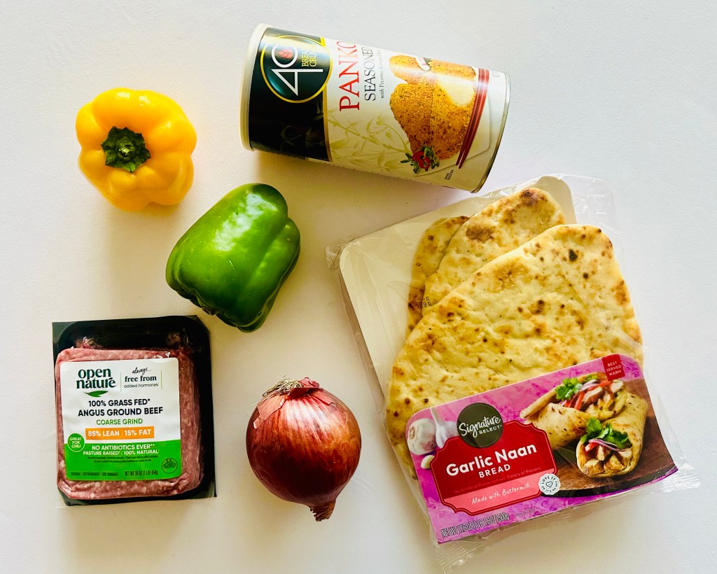 Ingredients for meatball kebabs including yellow and green bell peppers, red onion, packaged ground beef, garlic naan bread, and a can of seasoning.