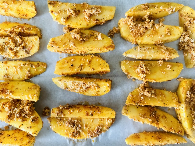 Potato wedges tossed with oil and spices on a baking sheet lined with parchment paper