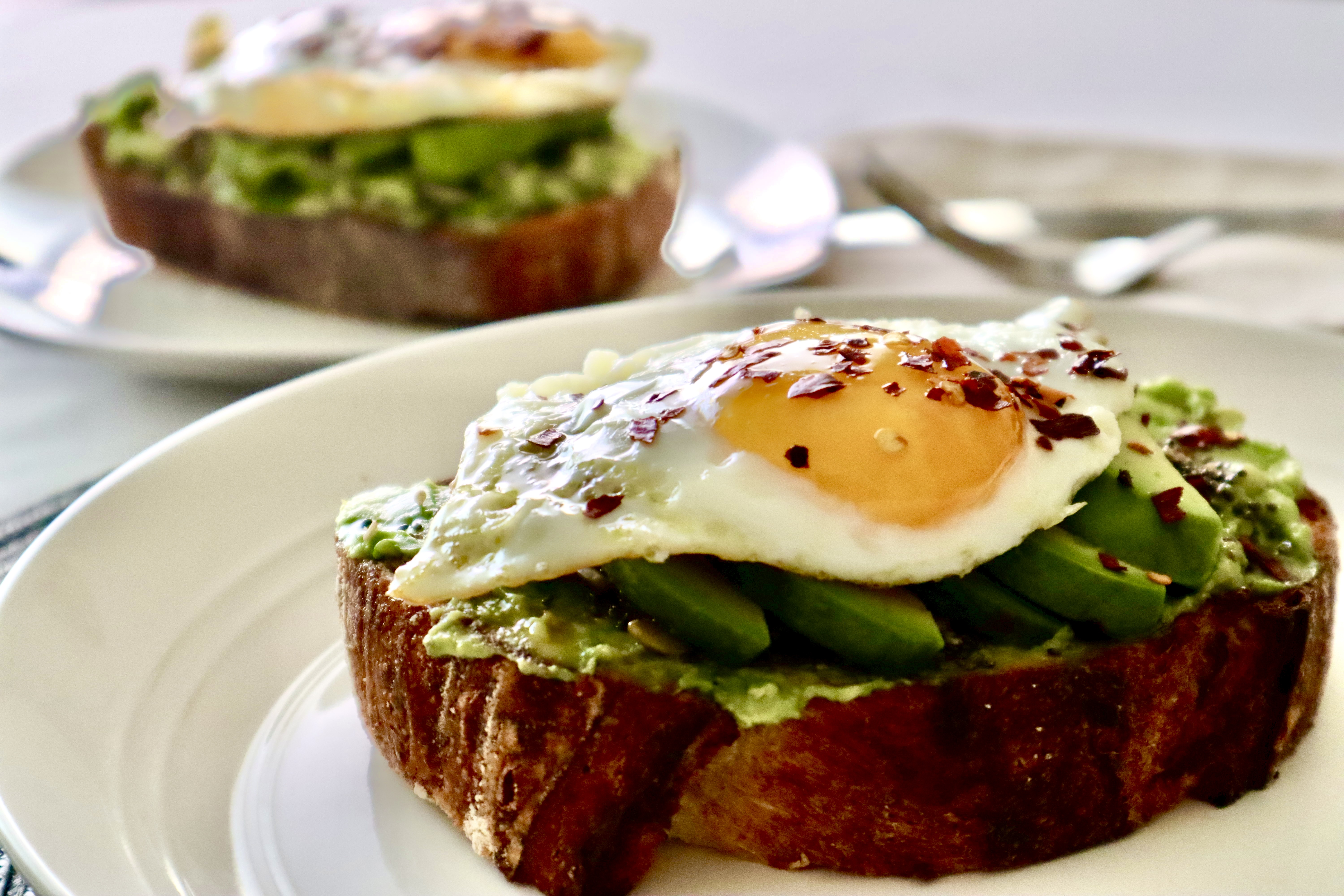 Sliced bread topped with mashed avocado, sliced avocado, and a fried egg.