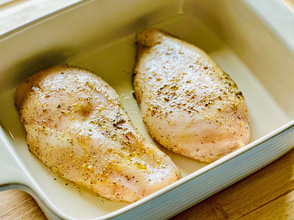 Uncooked chicken breasts seasoned with salt, pepper, oregano, and lemon pepper seasoning