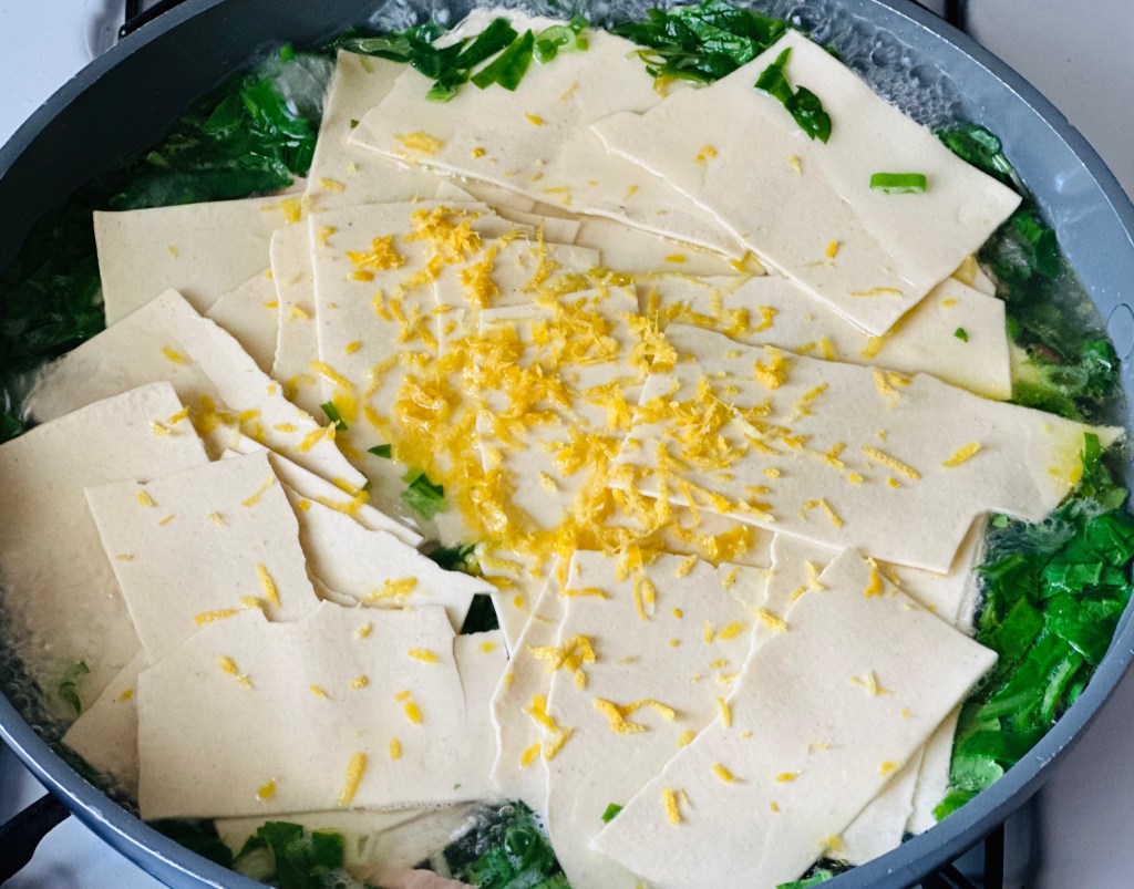 Frying pan of lasagna sheets, greens, and lemon zest