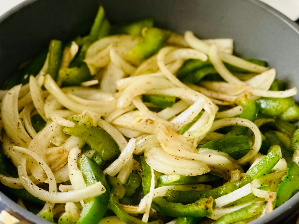 Sauteing onions and bell peppers in a pan