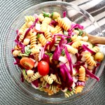 Clear glass bowl full of pasta, fresh vegetables, and chickpeas.