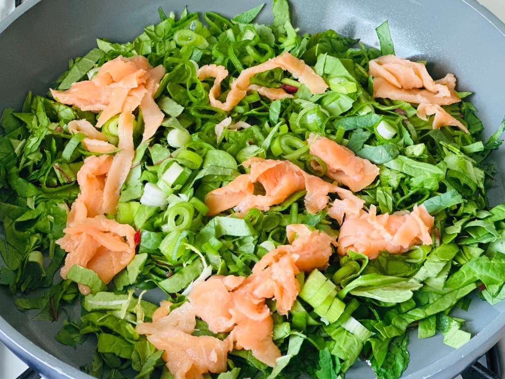 Frying pan full of scallions, mixed greens, and smoked salmon