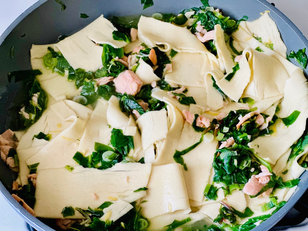 Pan with lasagna, smoked salmon, and greens submerged in boiling water