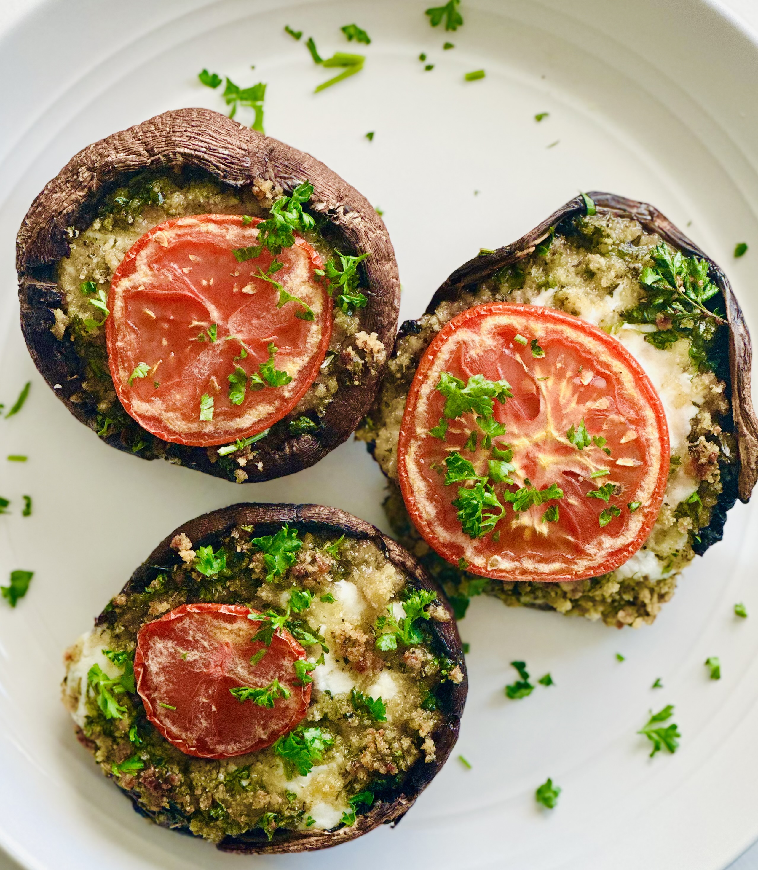 Serving plate of stuffed portobello mushrooms with mozzarella, tomato, parsley, garlic, panko, and Parmesan
