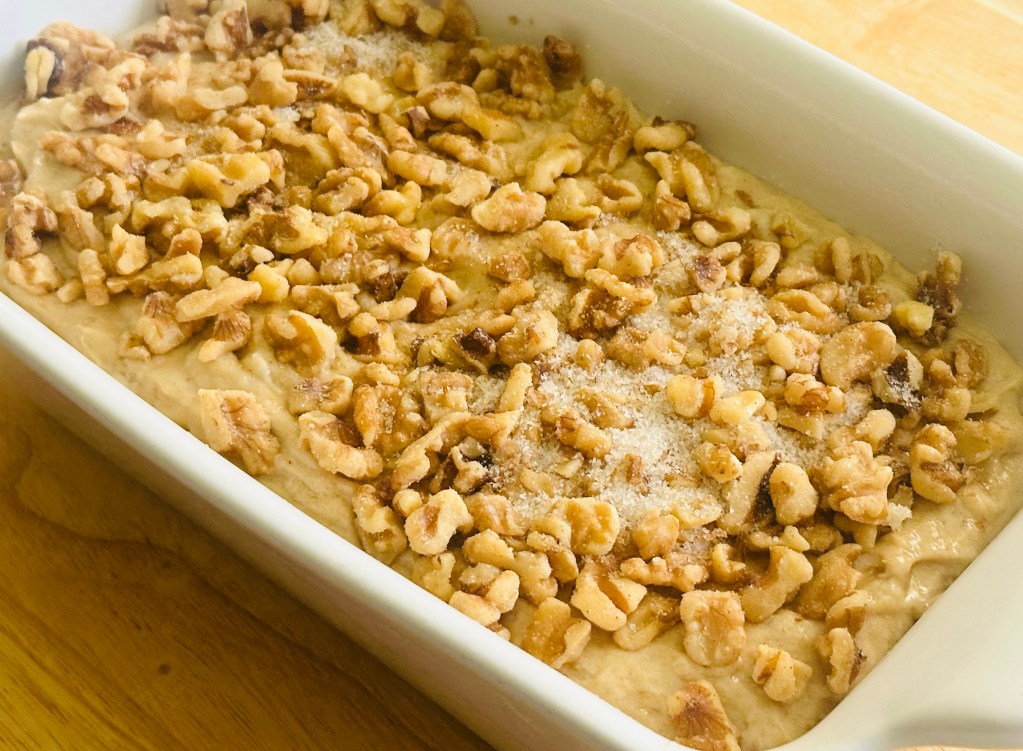 A loaf pan that's filled with banana bread batter and a topping of walnuts with cinnamon sugar