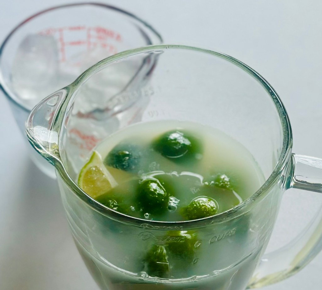 A blender full of quartered limes, sugar, condensed milk, and cold water