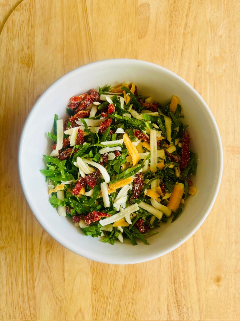 Bowl of chopped spinach, sun-dried tomatoes, and cheese