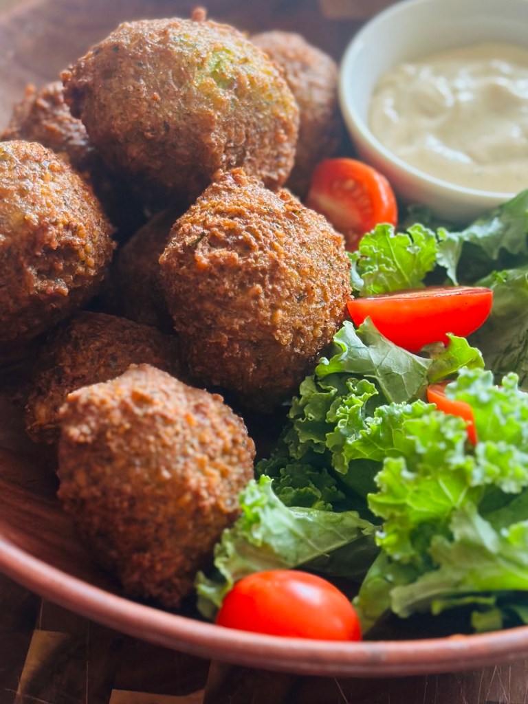 Fried falafel in a bowl with tahini sauce and a salad of lettuce and tomatoes