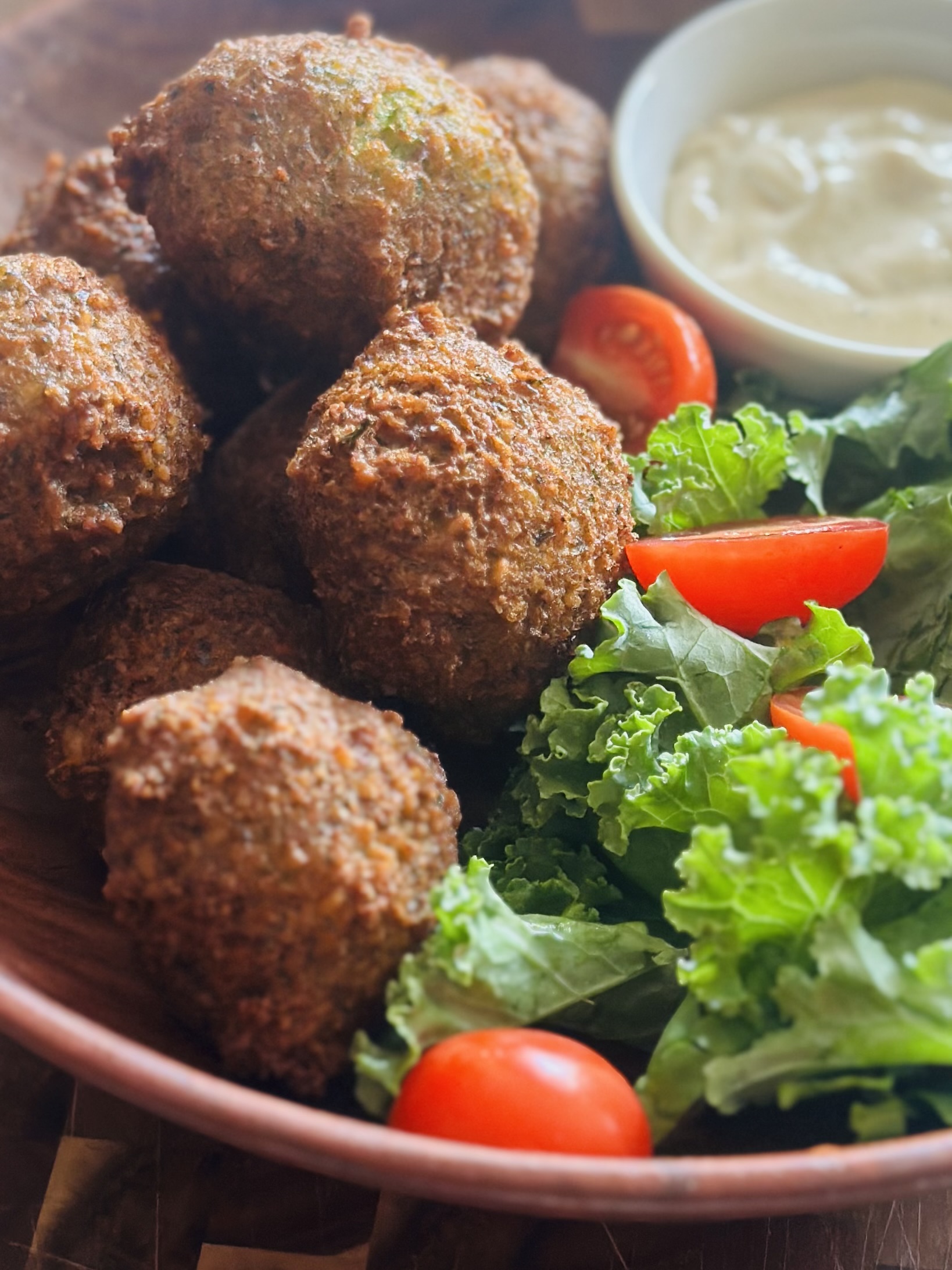 Fried falafel in a bowl with tahini sauce and a salad of lettuce and tomatoes
