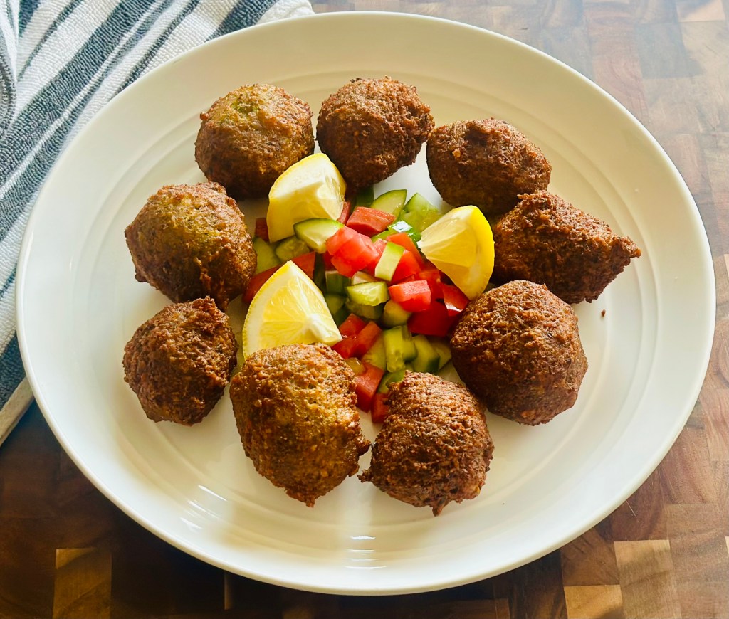 Fried falafel served on a plate with lemon slices and chopped cucumbers and tomatoes