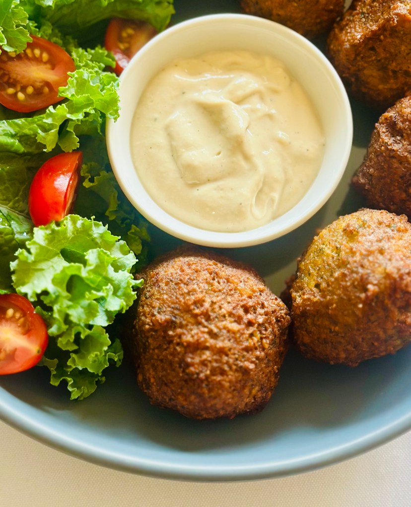 Fried falafel in a bowl with tahini sauce and a salad of lettuce and tomatoes