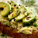 A slice of sourdough bread with egg salad and avocado slices on top