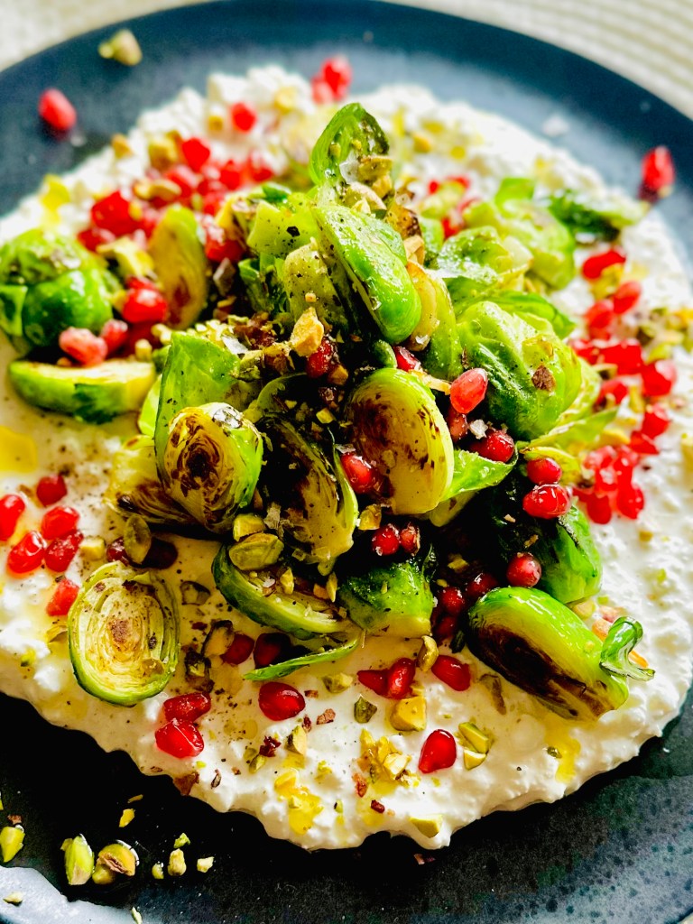 Crispy Brussels sprouts arranged on top of cottage cheese and sprinkled with pomegranate seeds and crushed pistachios