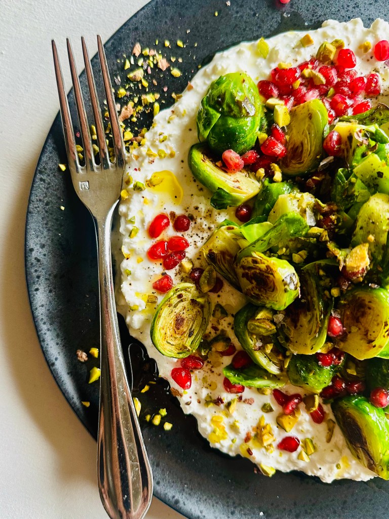Crispy Brussels sprouts arranged on top of cottage cheese and sprinkled with pomegranate seeds and crushed pistachios