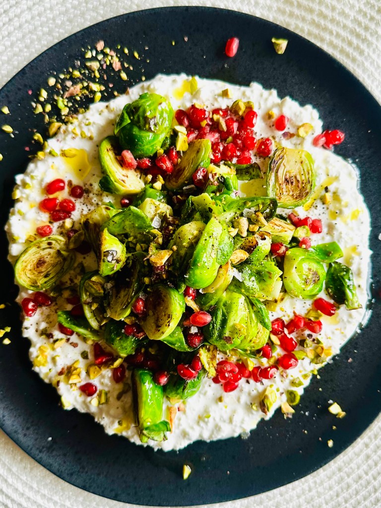 Crispy Brussels sprouts arranged on top of cottage cheese and sprinkled with pomegranate seeds and crushed pistachios