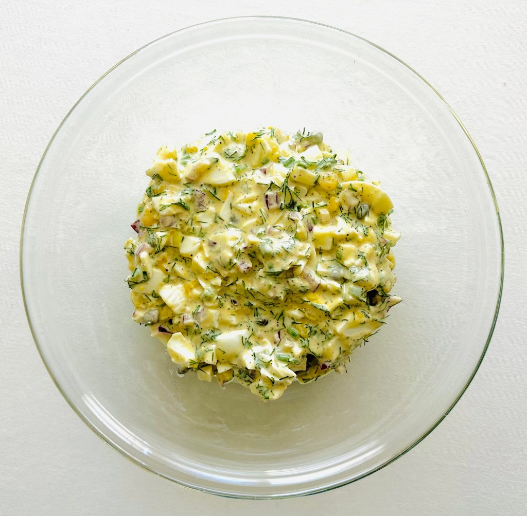 Egg salad ingredients mixed in a glass bowl