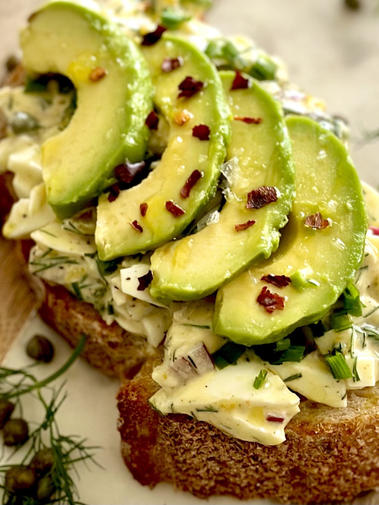 A slice of sourdough bread with egg salad and avocado slices on top