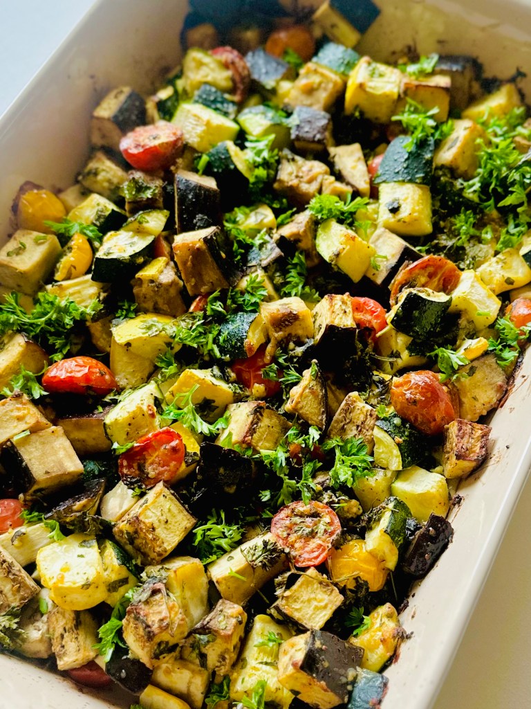Baked eggplant, zucchini, and tomato in a baking dish topped with grated Parmesan, basil, and parsley