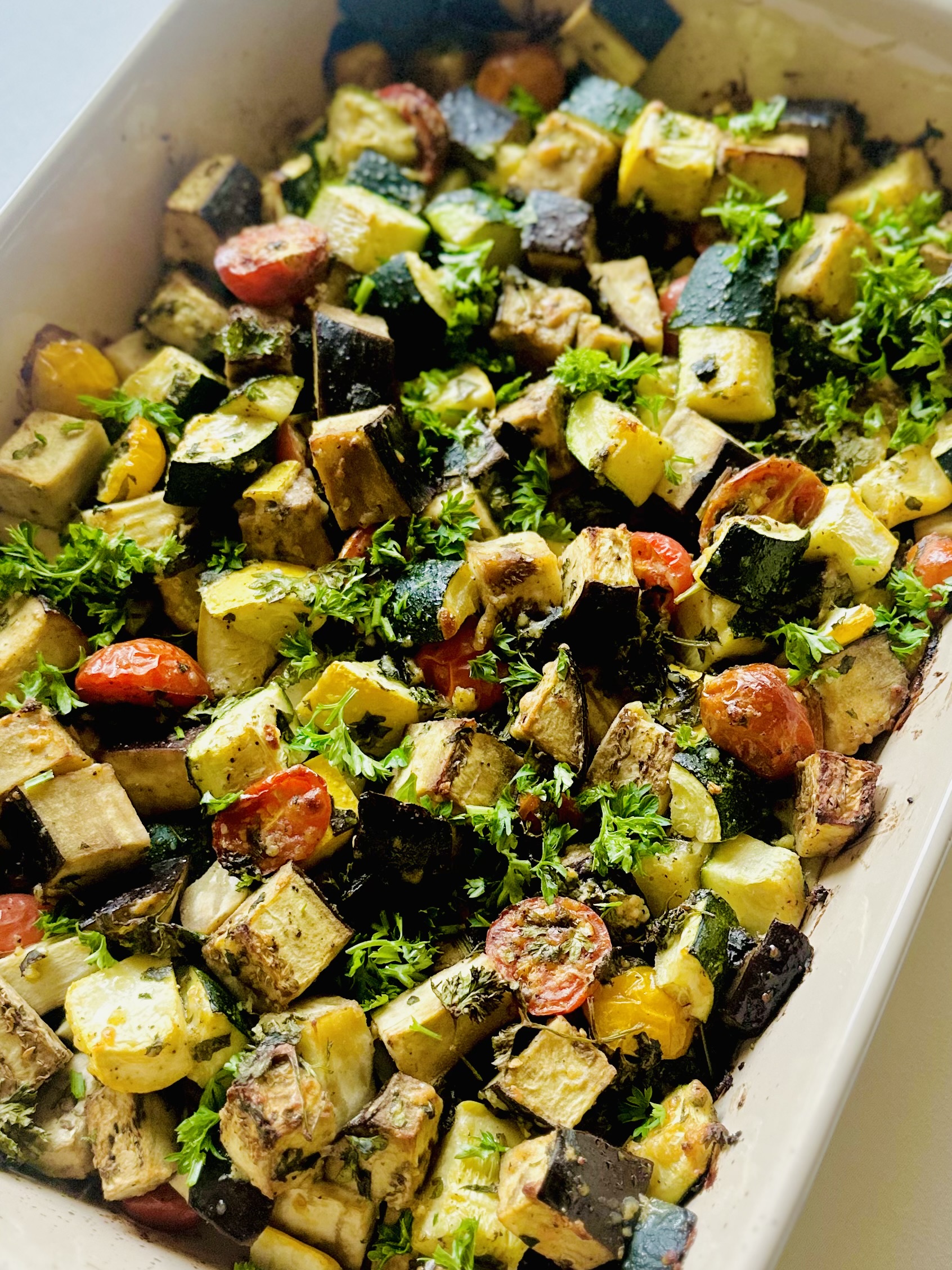 Baked eggplant, zucchini, and tomato in a baking dish topped with grated Parmesan, basil, and parsley