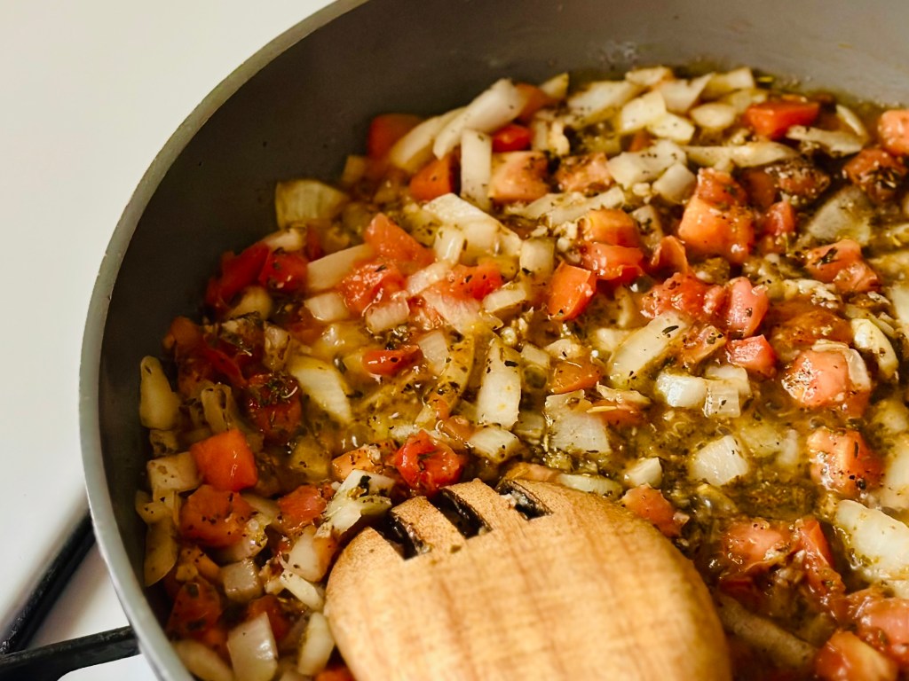 Frying pan with onion, garlic, and tomatoes being sauteed with seasonings