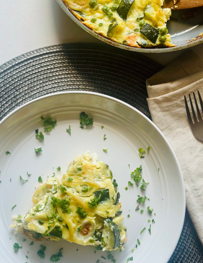 A slice of spaghetti frittata with zucchini and peas on a plate