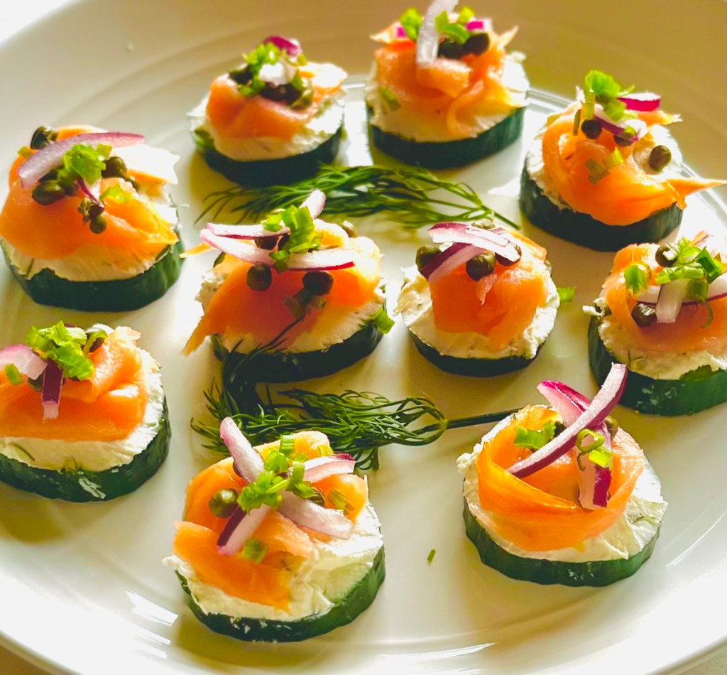 A serving plate full of smoked salmon, red onion, and capers on a bed of cream cheese atop cucumber slices