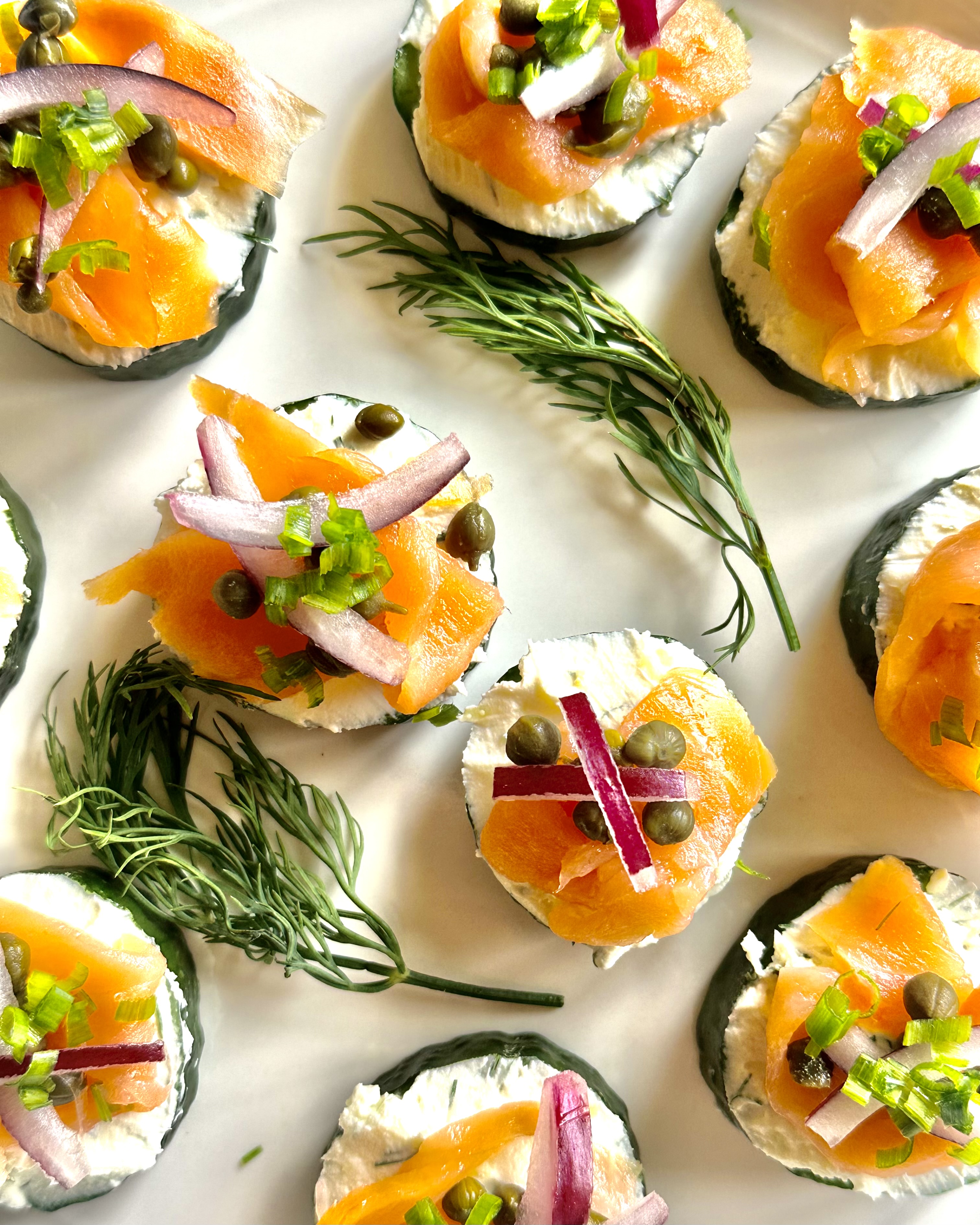 A serving plate full of smoked salmon, red onion, and capers on a bed of cream cheese atop cucumber slices
