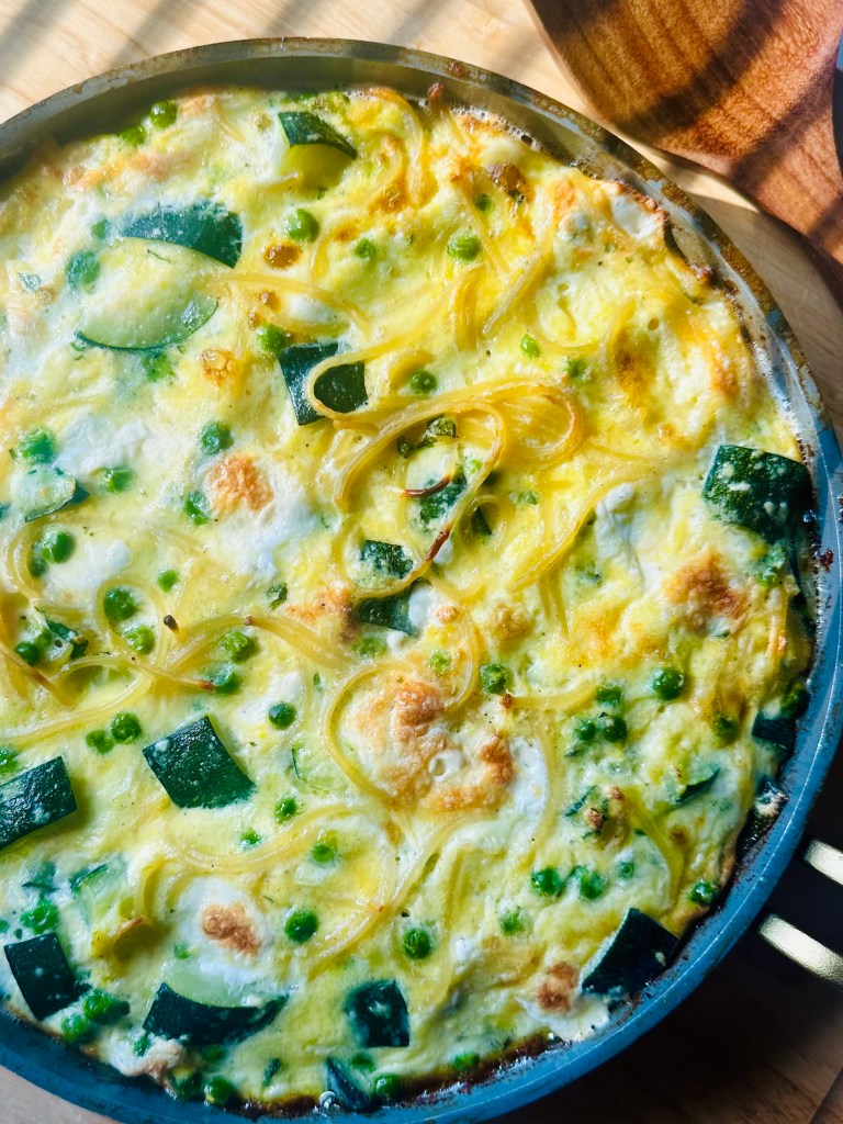 Baked spaghetti frittata with zucchini and peas in a frying pan