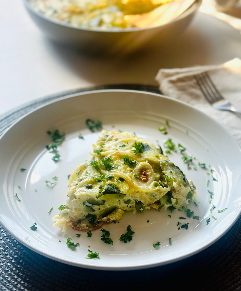A slice of spaghetti frittata with zucchini and peas on a plate