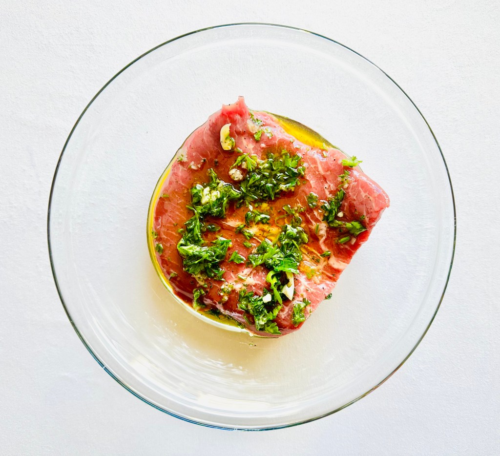 A glass bowl with a piece of flat iron steak inside and marinade drizzled on top