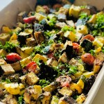 Baked eggplant, zucchini, and tomato in a baking dish topped with grated Parmesan, basil, and parsley