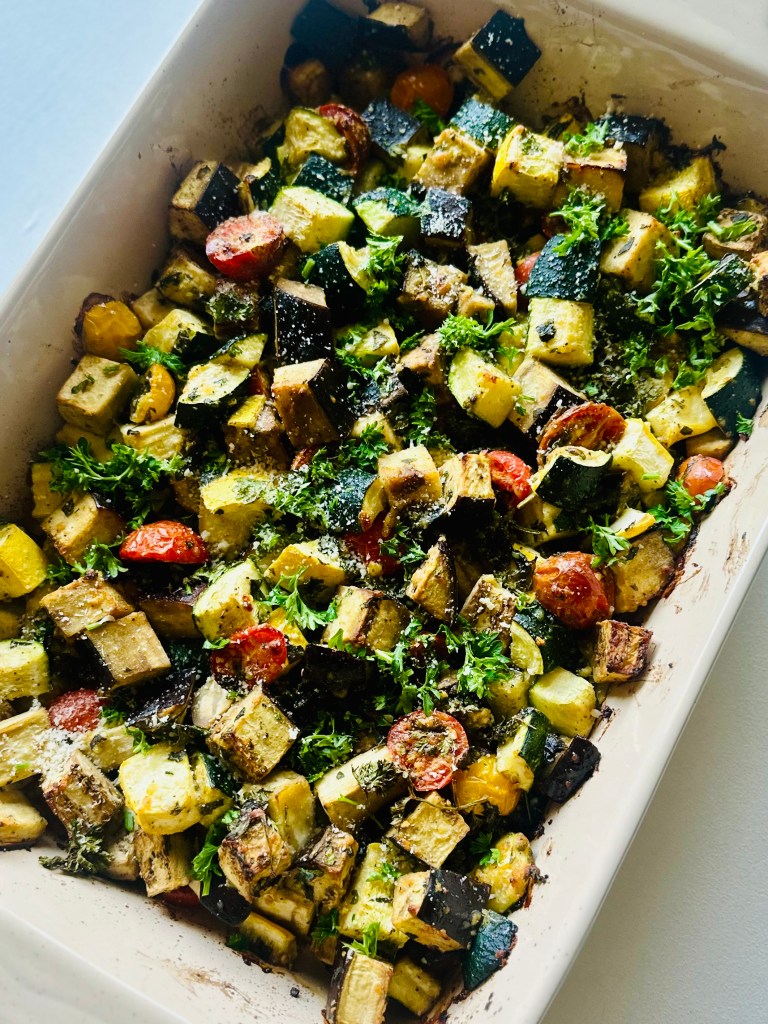 Baked eggplant, zucchini, and tomato in a baking dish topped with grated Parmesan, basil, and parsley