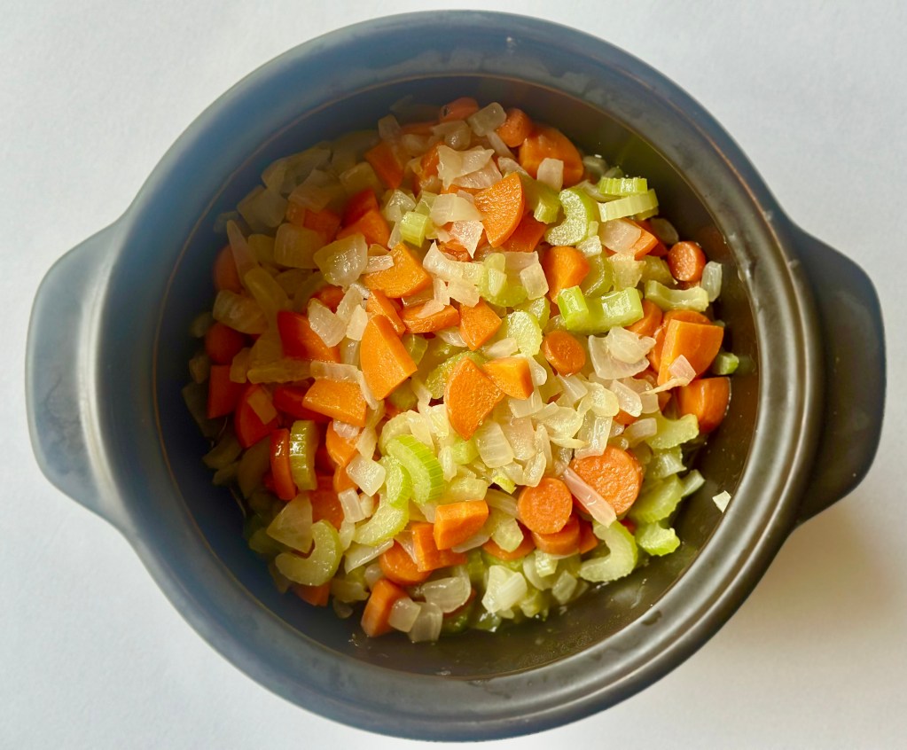 A soup pot full of onions, carrots, and celery being sauteed in butter