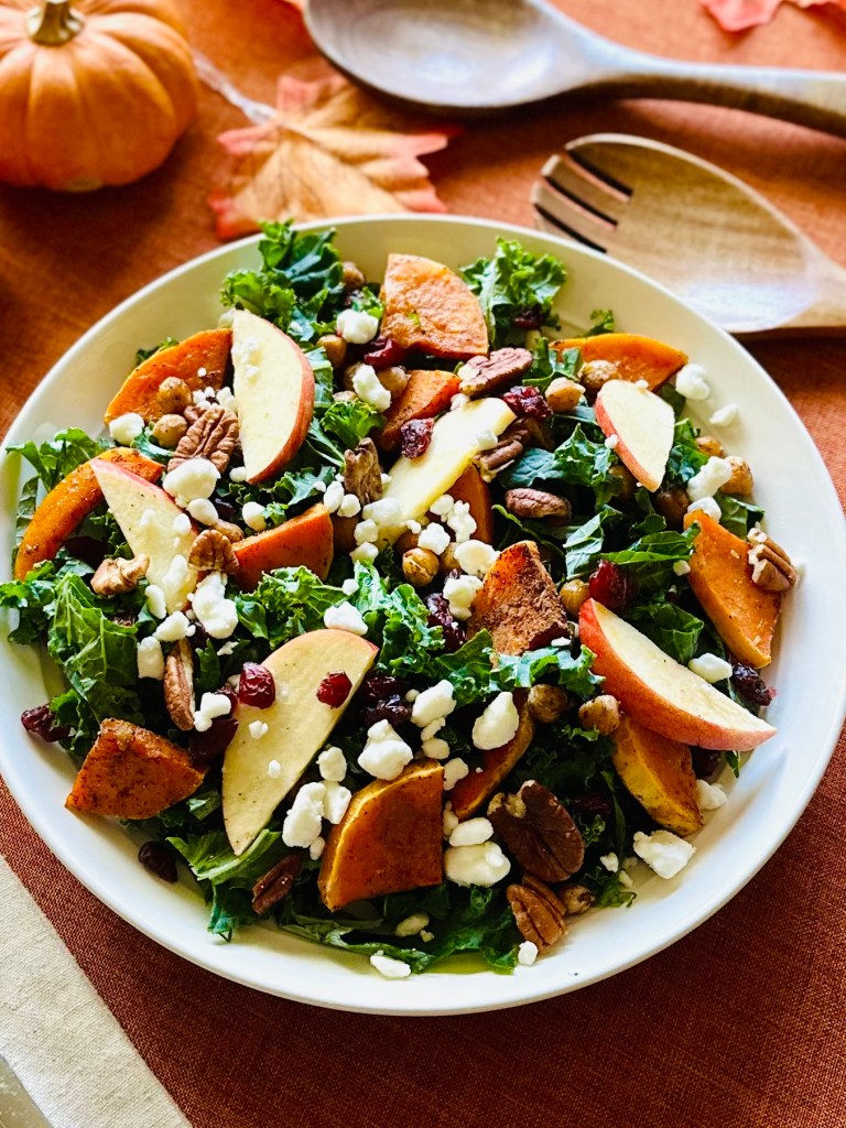 A serving plate with kale, roasted butternut squash and chickpeas, apple slices, pecans, and goat cheese