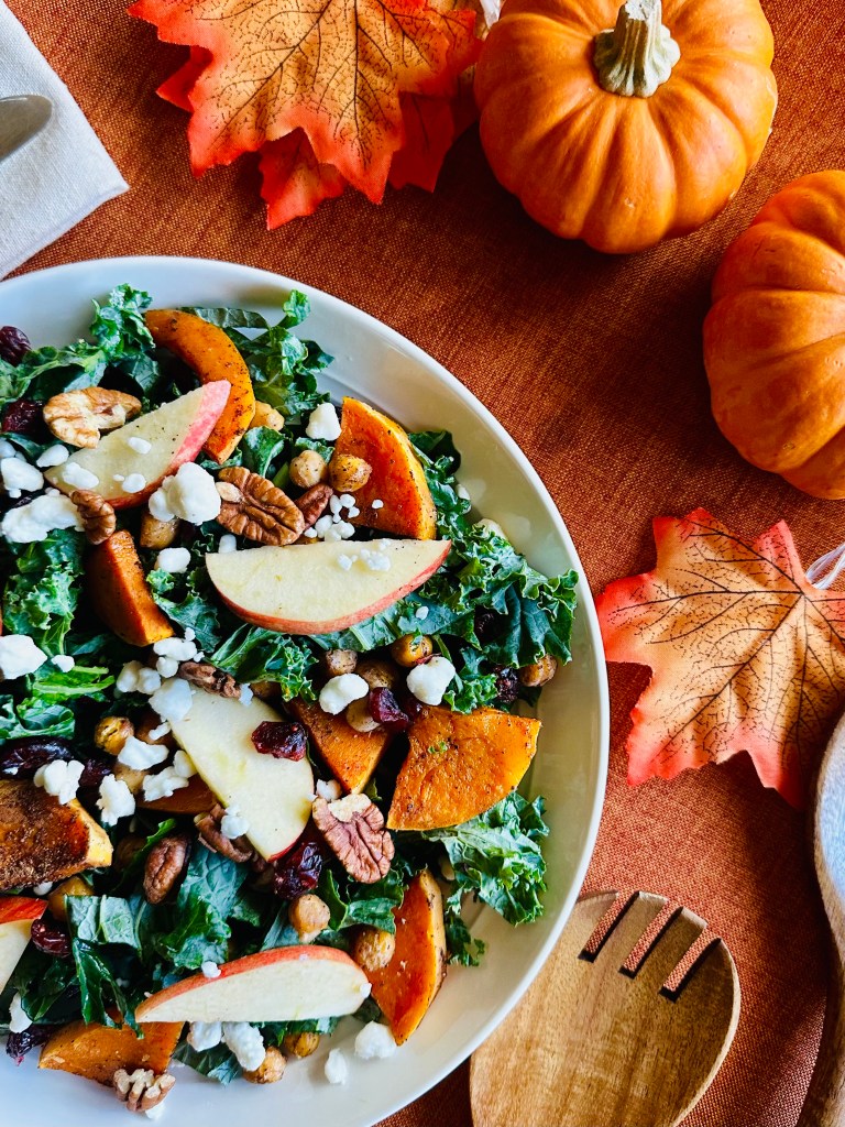 A serving plate with kale, roasted butternut squash and chickpeas, apple slices, pecans, and goat cheese