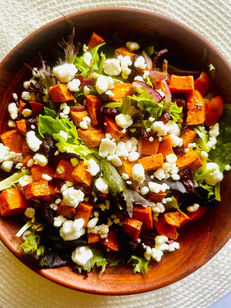 A salad of roasted sweet potatoes and red onion, mixed greens, feta, and dried cranberries