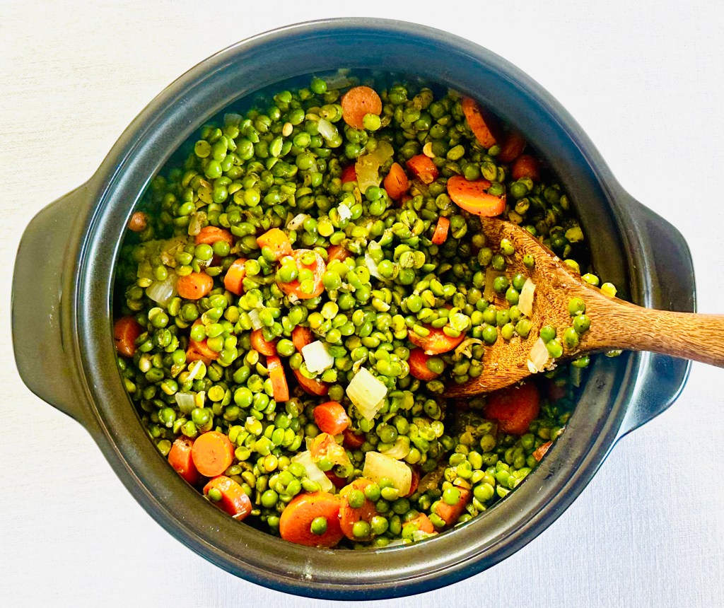 A pan with green lentils, carrots, onion, garlic, and spices being cooked together