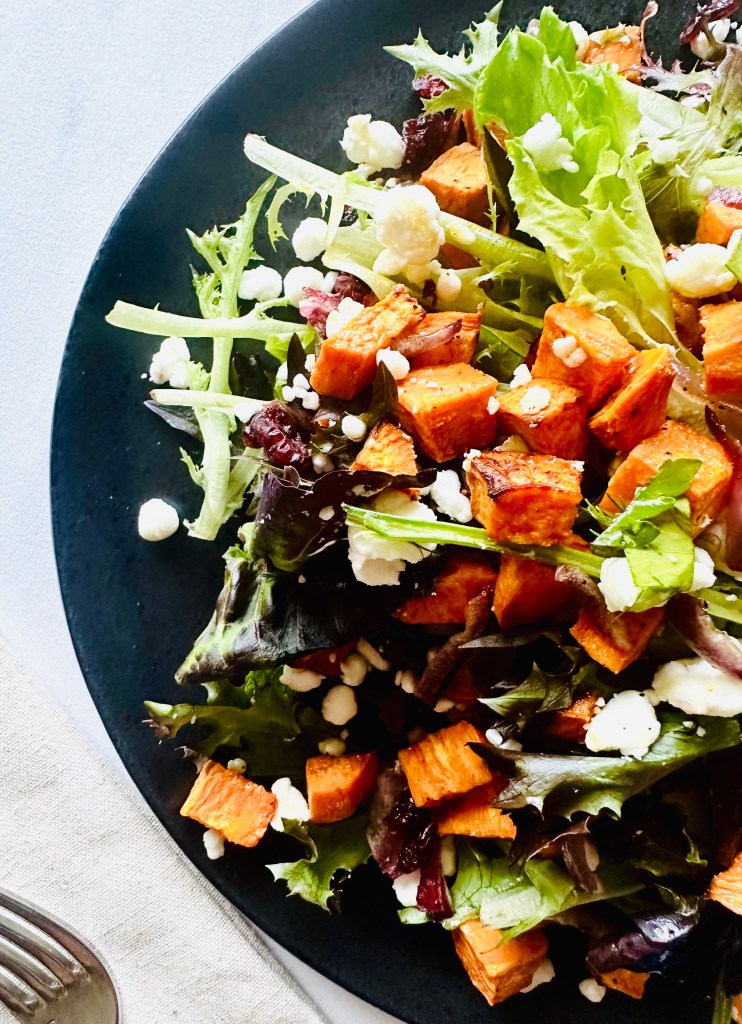 A salad of roasted sweet potatoes and red onion, mixed greens, feta, and dried cranberries
