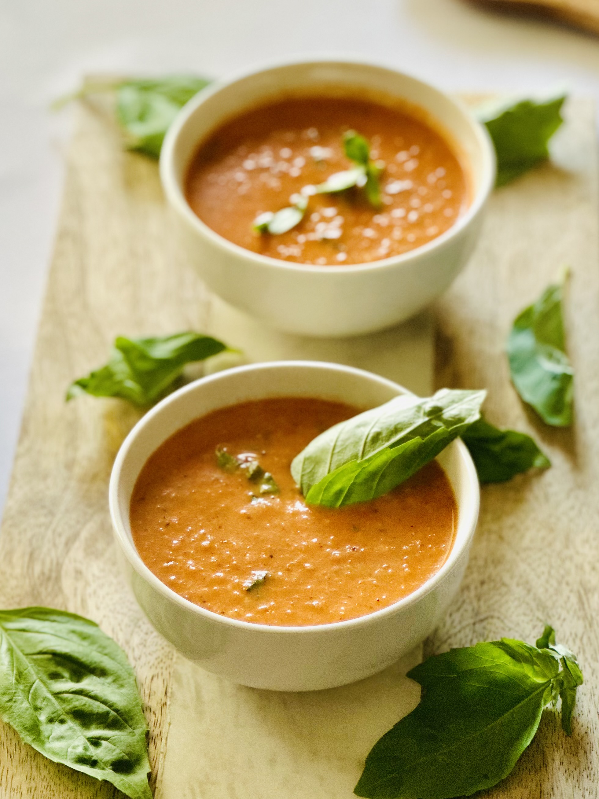 A photo of tomato basil soup ladled out in bowls with a garnish of fresh basil leaves