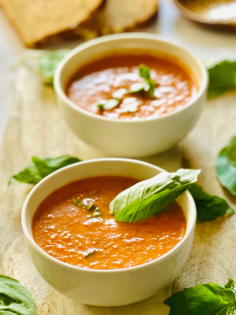 A photo of tomato basil soup ladled out in bowls with a garnish of fresh basil leaves